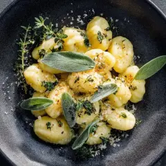 Salbei Gnocchi mit frischen Kräutern und Parmesan bestreut, serviert auf einem dunklen Teller.