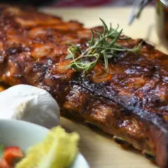 Soczyste żeberka w piekarniku, idealne do marynaty. Obok sos BBQ, czosnek i świeże zioła.
