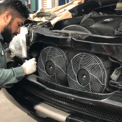 Mechanik w białych rękawiczkach sprawdza wentylatory chłodnicy samochodu.
