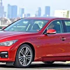 Czerwony infiniti samochód z kierowcą za kierownicą, na tle miejskiej panoramy.