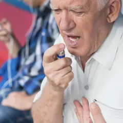 Starszy mężczyzna z bólem w klatce piersiowej używa sprayu z nitrogliceryną.