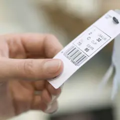 Main d'une personne tenant une étiquette de vêtement avec un code-barres et des tailles.