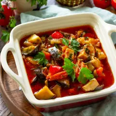 Pyszny gulasz z kurczaka z bakłażanem i papryką, udekorowany natką pietruszki. Aromatyczne danie w białej zapiekance.