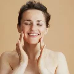 Kobieta z zamkniętymi oczami nakłada peeling na twarz, ciesząc się zabiegiem. Zastanawiasz się, jak często robić peeling twarzy?
