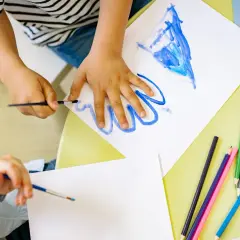 Manos de niños pintando con acuarelas y lápices de colores, aprendiendo los lomloe saberes básicos.