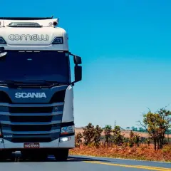 Biała ciężarówka Scania z naczepą jedzie po pustej drodze, zapowiadając zasłużoną pauzę weekendową.