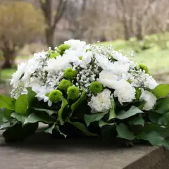 Białe i zielone kwiaty, jakby stworzone na listopadowe zaduszki, spoczywają na kamiennym postumencie.