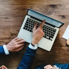 Biznesmen wypełnia wniosek o pozwolenie (application for permit) na laptopie. Obok leżą dokumenty i telefon.