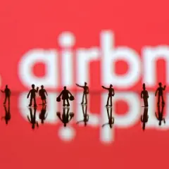 Małe figurki ludzi na tle logo Airbnb. Zastanawiasz się, airbnb co to? To platforma do rezerwacji noclegów i doświadczeń.
