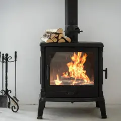 Ein brennender Holzofen mit Holzscheiten und einem Fächer zur Steigerung des holzofen wirkungsgrad. Daneben ein Kaminbesteck.
