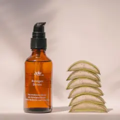 Braunes Fläschchen mit Rotalgen Serum, das Rotalgenextrakt als geliermittel enthält, neben aufgestapelten Aloe-Vera-Scheiben.