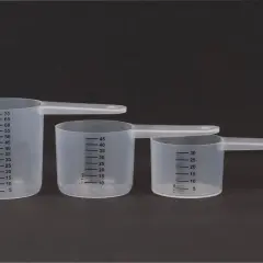 Trzy plastikowe miarki kuchenne z podziałką w mililitrach na ciemnym tle.