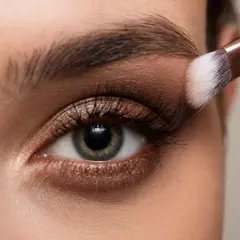 Occhio con trucco elegante, sfumature bronze e un pennello che applica l'ombretto.