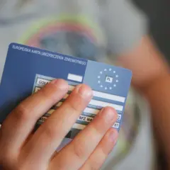 Dziecko trzyma Europejską Kartę Ubezpieczenia Zdrowotnego. Czasem warto sprawdzić, ile się czeka na wizytę, gdy ma się EKUZ.