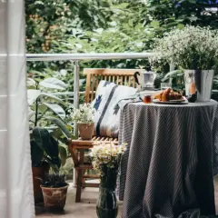 Gemütlich einen kleinen Balkon einrichten: Frühstück mit Croissant und Kaffee auf dem Tisch, umgeben von Pflanzen.