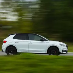Un Skoda Fabia 130 blanco con techo negro se mueve rápido por una carretera rural, con el paisaje difuminado por la velocidad.
