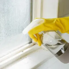 Main jaune pulvérisant un produit sur une fenêtre en aluminium sale après un chantier.
