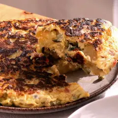 Una porción de tortilla paisana, dorada y jugosa, se levanta con un tenedor, revelando patatas, pimientos y huevo.