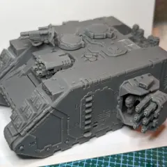 Szary model Land Raider Redeemer, gotowy do malowania, z działkiem na dachu i wyrzutniami flamerów po bokach.