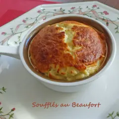 Un délicieux soufflé au beaufort, doré et gonflé, servi dans un ramequin sur une assiette décorée de rubans et de fleurs.