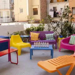 Un colorido conjunto de muebles de terraza, listo para pintar. Sillas, bancos y mesas en vibrantes tonos, con latas de spray dispuestas para dar vida a este espacio exterior.