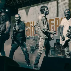 La band "Asilo Republic" sul palco, con chitarristi e cantante in azione, avvolti dal fumo.