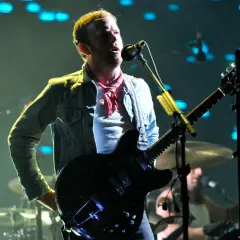 Wokalista Kings of Leon Polska na koncercie, gra na gitarze elektrycznej, w dżinsowej kurtce i czerwonej chuście.