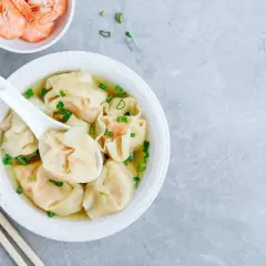 Aksamitna zupa wonton z krewetkami i szczypiorkiem, podana z pałeczkami.