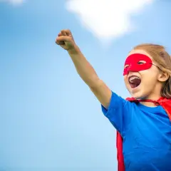 Ein Kind im Superhelden-Kostüm mit rotem Cape und Maske, bereit für den ablauf einschulung.