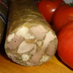 Kawałek salcesonu z widocznymi mięsem i galaretą, obok dojrzałe pomidory. Zastanawiasz się, jak długo parzyć salceson?