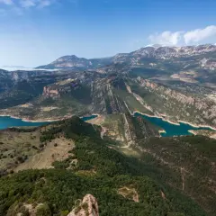 Paisaje montañoso con embalses de agua turquesa, ideal para explorar rutas Pirineos. Bosques verdes cubren las laderas y picos nevados al fondo.
