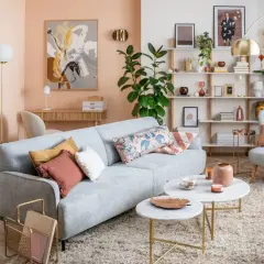 Soggiorno accogliente con divano grigio, cuscini decorativi e tavolini in marmo. Le pareti color pesca e gli arredi creano un'atmosfera rilassante, mostrando come i **colori pastello quali sono** perfetti per un ambiente sereno.