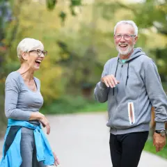 Ein lachendes älteres Paar genießt einen Spaziergang im Park. Bewegung hält sie geistig fit und glücklich.