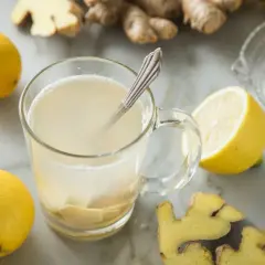 Ein Glas mit warmem tee ingwer, umgeben von frischen Zitronen und Ingwerwurzeln.