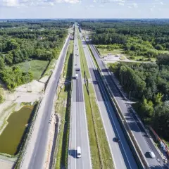 Szeroka autostrada S7 Warszawa-Grójec, otoczona lasami, z kilkoma samochodami w ruchu.
