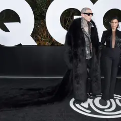 Travis Barker i jego żona Kourtney Kardashian na ściance GQ. Travis w ekstrawaganckim futrze, Kourtney w eleganckim garniturze.