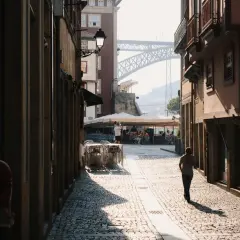 A lone figure walks down a sun-drenched cobblestone street in a European city, a perfect scene for street photography.