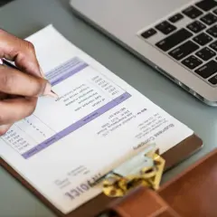 Person schreibt Rechnung. Möglicherweise sind umzugskosten steuerlich absetzbar. Laptop und Notizbuch liegen daneben.