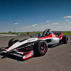 Wyścigowy bolid, przypominający co to f1, pędzi po torze. Czerwono-białe malowanie i logo "Prezentmarzeń" zdobią jego karoserię.