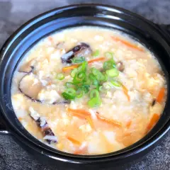 A comforting bowl of Japanese rice soup, also known as okayu, filled with tender rice, shiitake mushrooms, shredded carrots, and scrambled egg, garnished with fresh green onions.