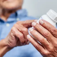 Ältere Hände halten eine Pillendose. Die Glucosamin Wirkung für Gelenke wird hier thematisiert.