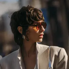 Frau mit einem frechen Pixie Cut, Sonnenbrille und Blazer.