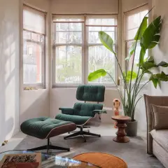Gemütlicher mid century modern living room mit dunkelgrünem Sessel und Hocker, großem Fenster und einer Strelitzie.