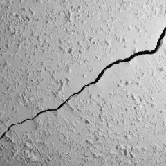 Une fissure traverse le plafond texturé d'un appartement, révélant une ombre profonde.