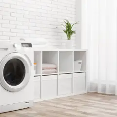 Weiße Waschmaschine mit beladener Trommel steht neben einem Regal mit Handtüchern und Aufbewahrungsboxen. Die Waschmaschine wandert nicht, sie steht fest.
