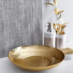 Un bol texturé doré, un distributeur de savon et une barre de savon sur un comptoir blanc, évoquant une ambiance de douche dorée.