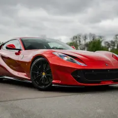 Czerwony, luksusowy samochód sportowy Ferrari 812 Superfast na tle pochmurnego nieba i zieleni.