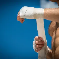 A boxer wraps his hands, preparing for a fight under a bright blue sky.