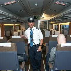 Pracownik kolei w mundurze stoi w pustym wagonie. Może to być pierwszy krok, jak zostać kierownikiem pociągu.