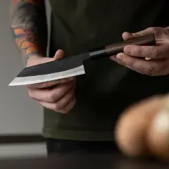 Manos sostienen un cuchillo de chef con hoja de acero VG10, listo para cortar.